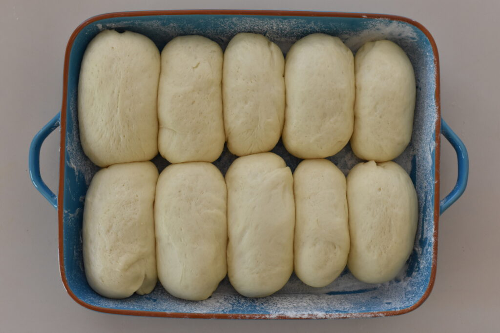 Risen dough buns sitting in dusted tray.