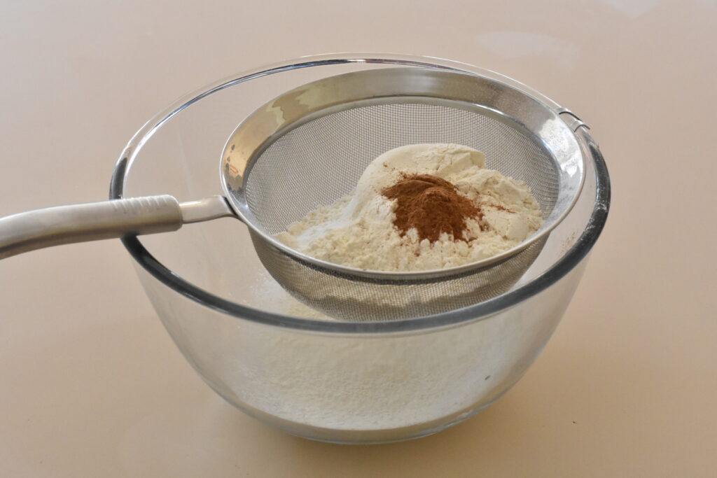Flour, salt and spices in a sifter over bowl.