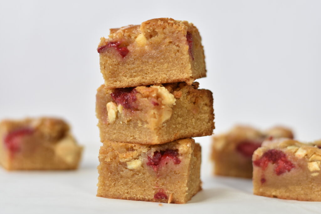 Stack of three squares of white chocolate and raspberry blondies.