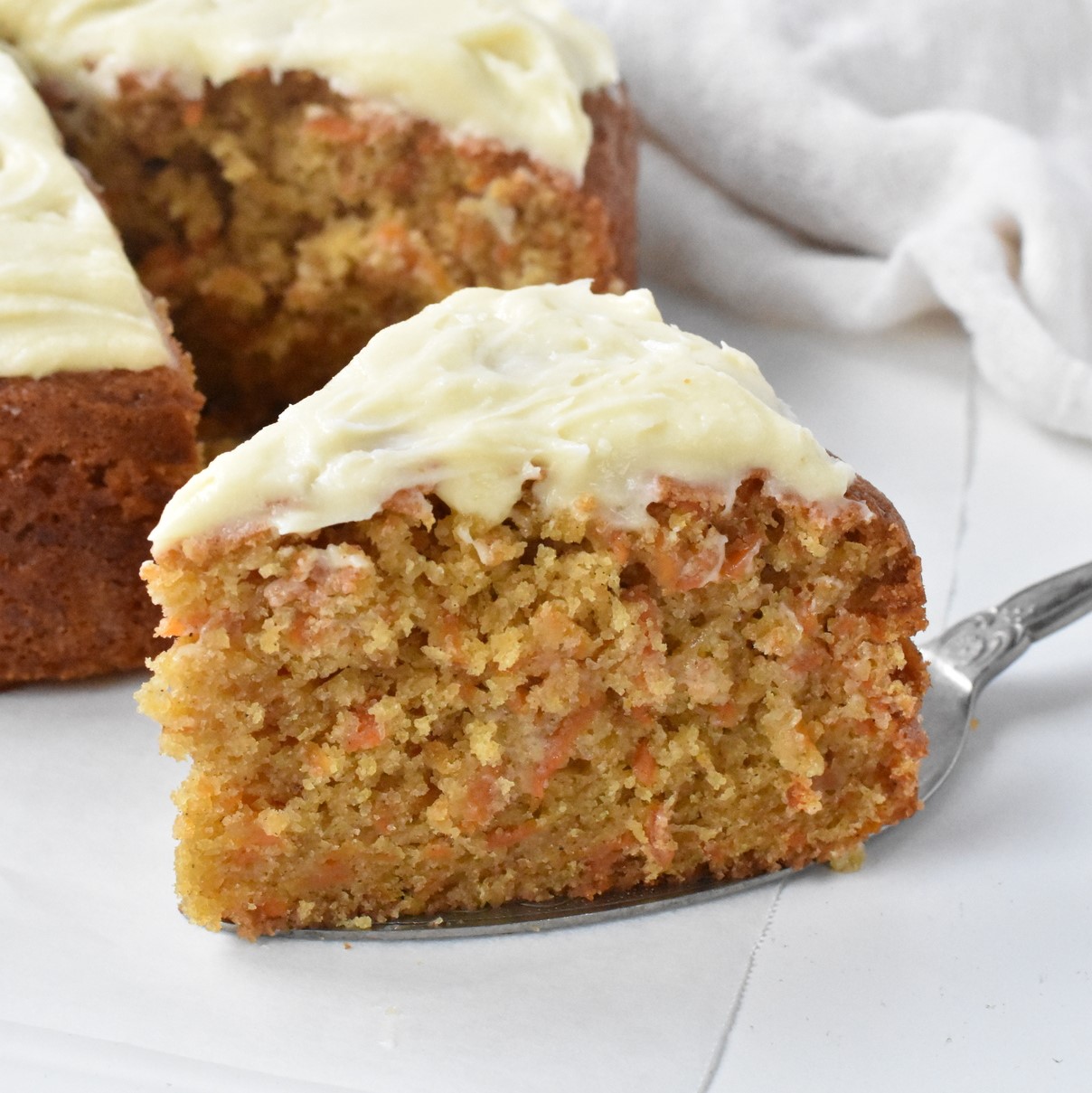 Slice of carrot cake with cream cheese frosting on cake server.