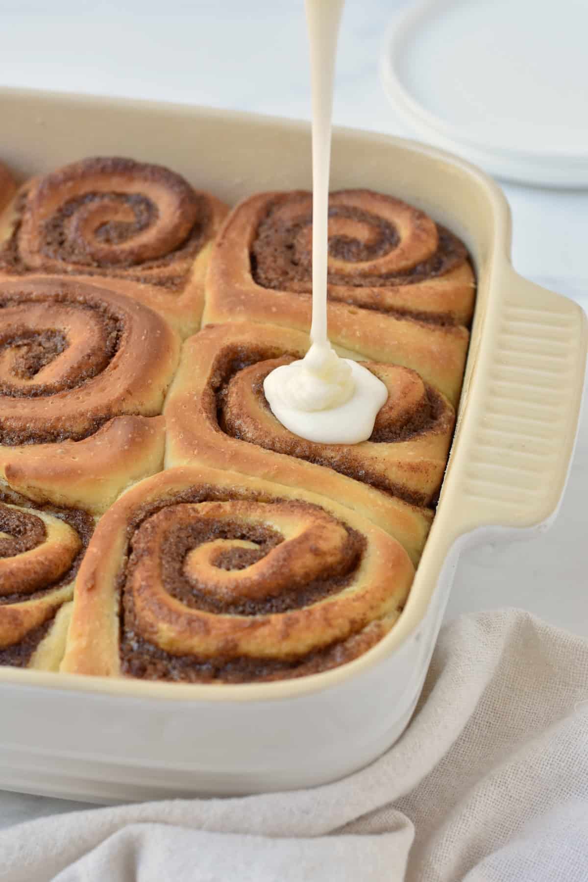 Glaze being poured over cinnamon rolls