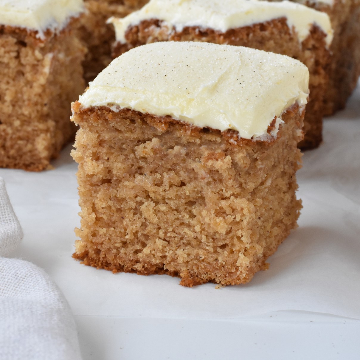 Square of spice cake with frosting on baking paper.