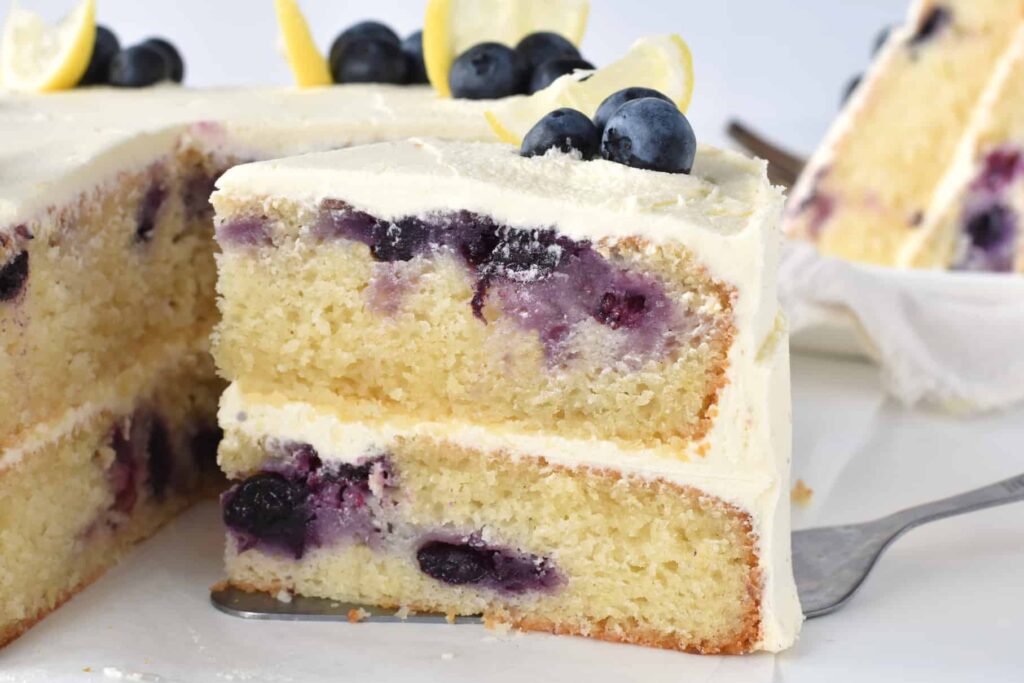 Slice of lemon blueberry cake in front of whole cake.