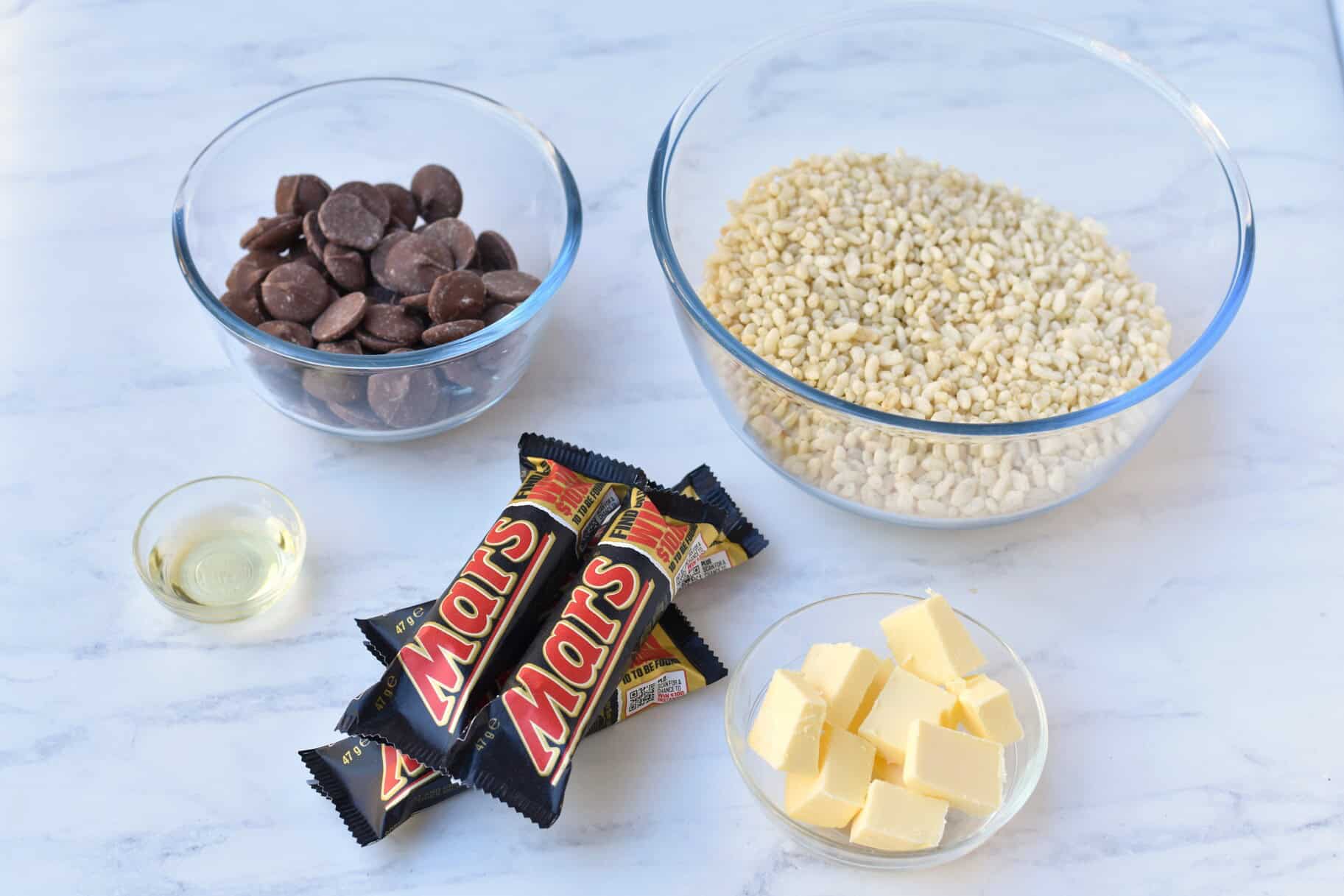 Chocolate melts, rice bubbles, oil, mars bars and butter in separate bowls.