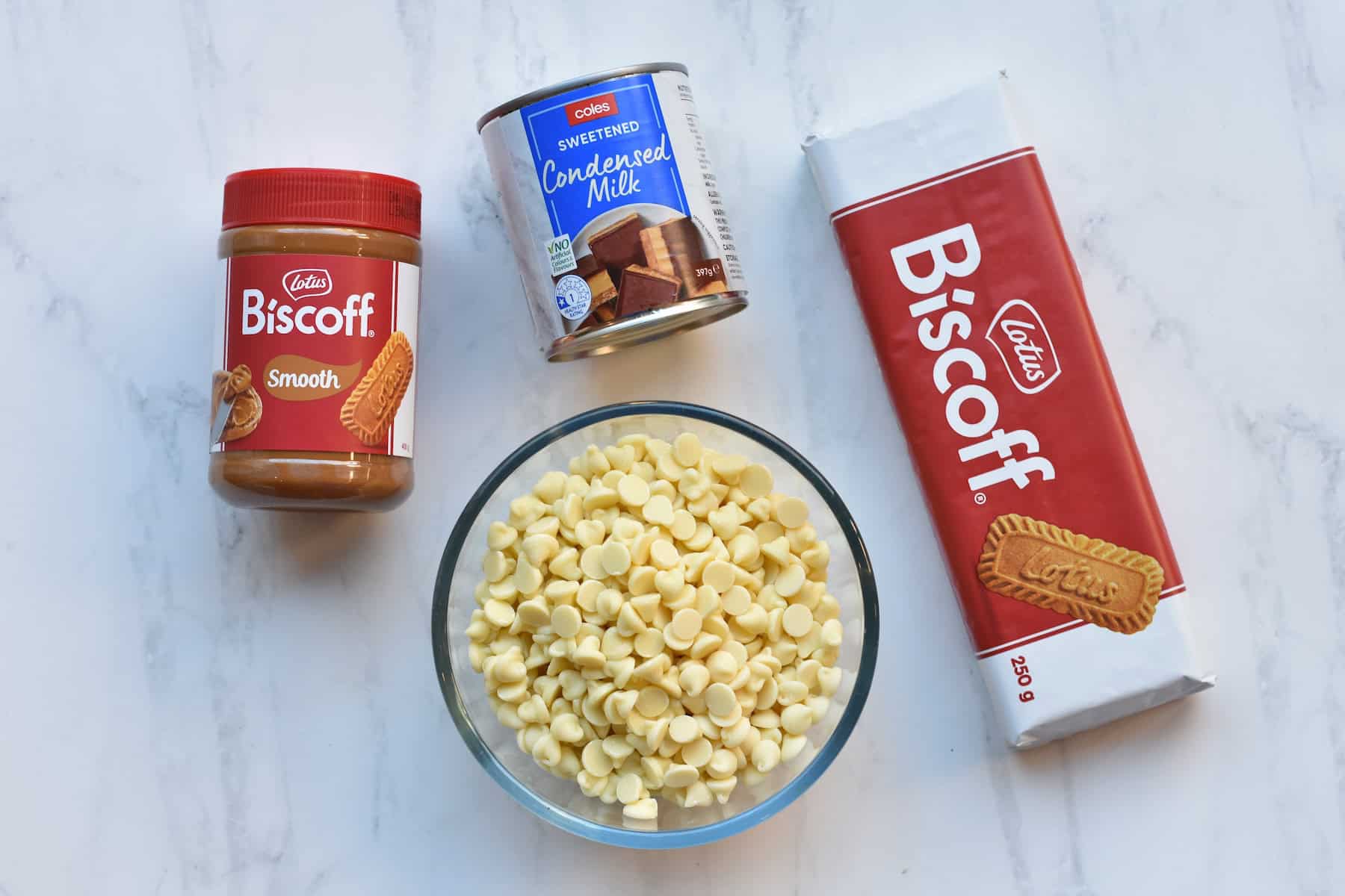 Biscoff spread, condensed milk can, biscoff cookies packet and white choc chips in a bowl.