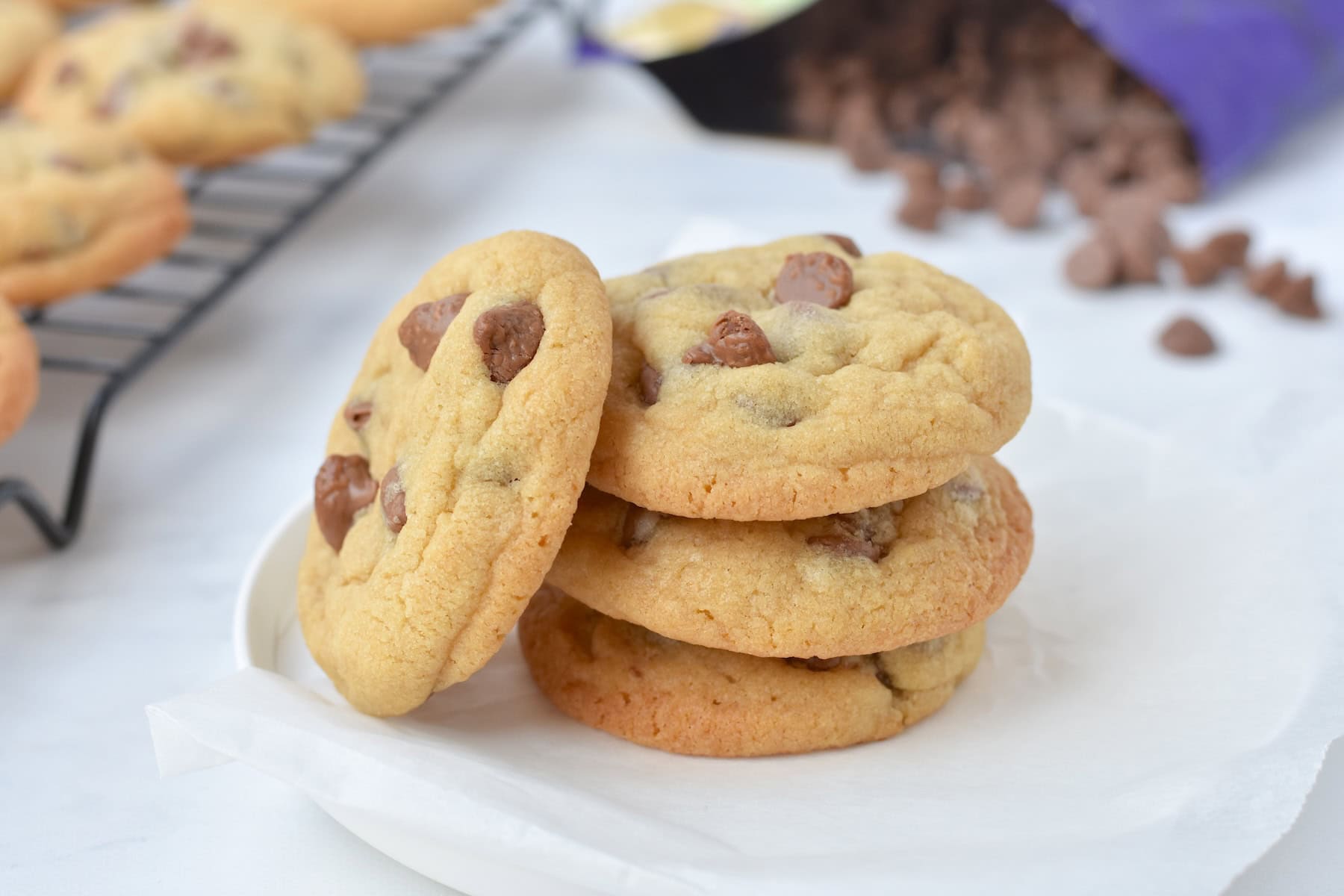 Stack of three cookies on a plate with a cookie leaning on them.