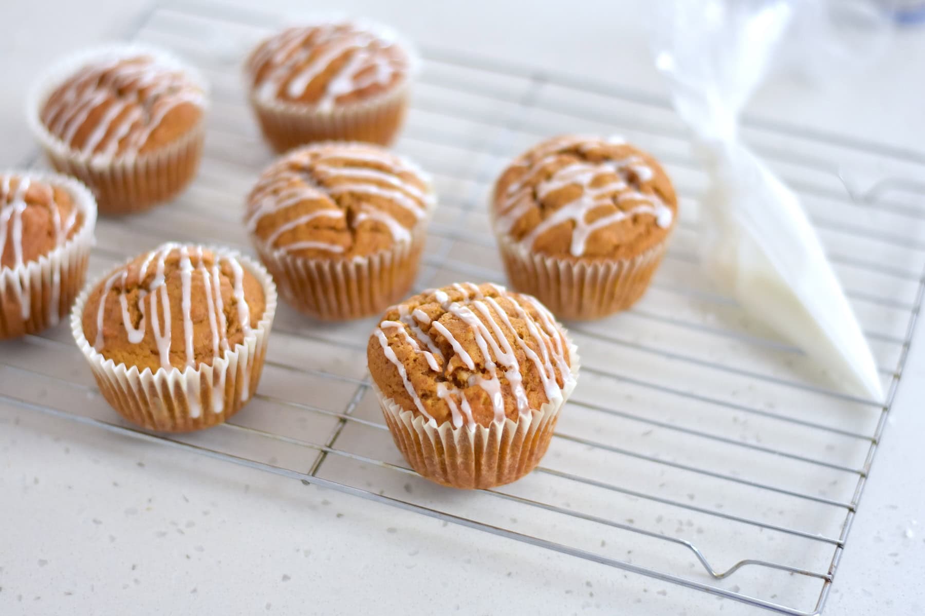 Pumpkin muffins with white glaze on wire rack.