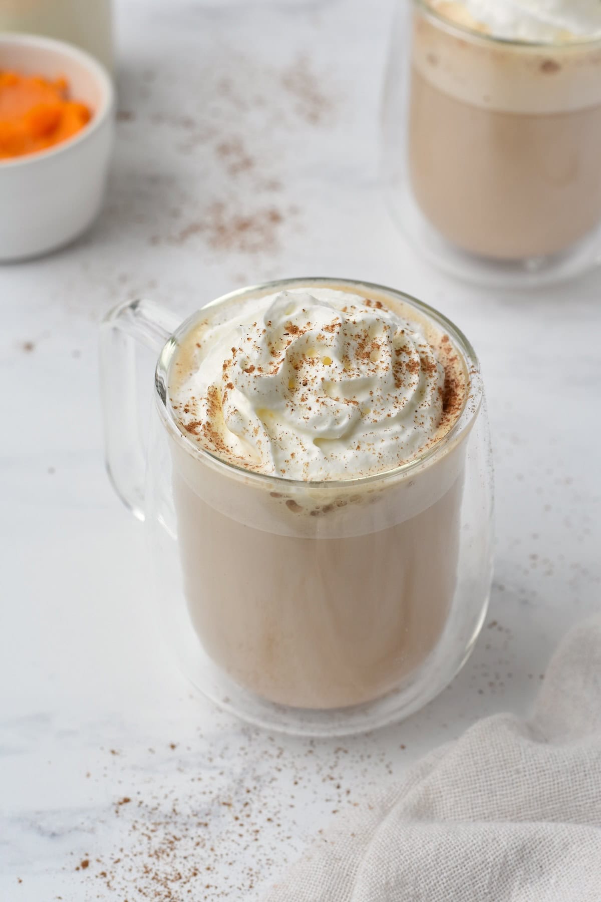Pumpkin spice latte in glass cup with whipped cream on top.