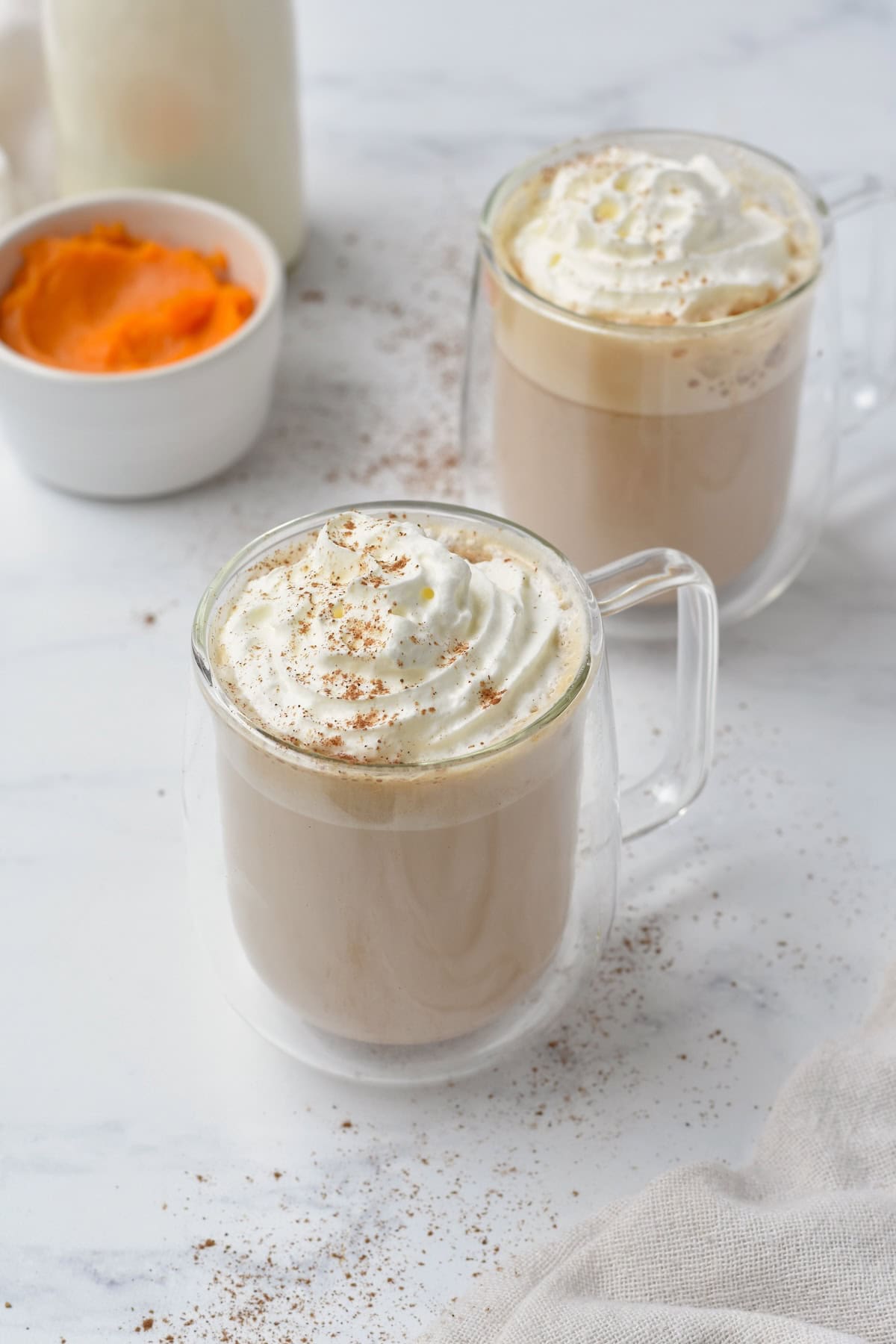 Pumpkin spice latte in glass cup with whipped cream on top.