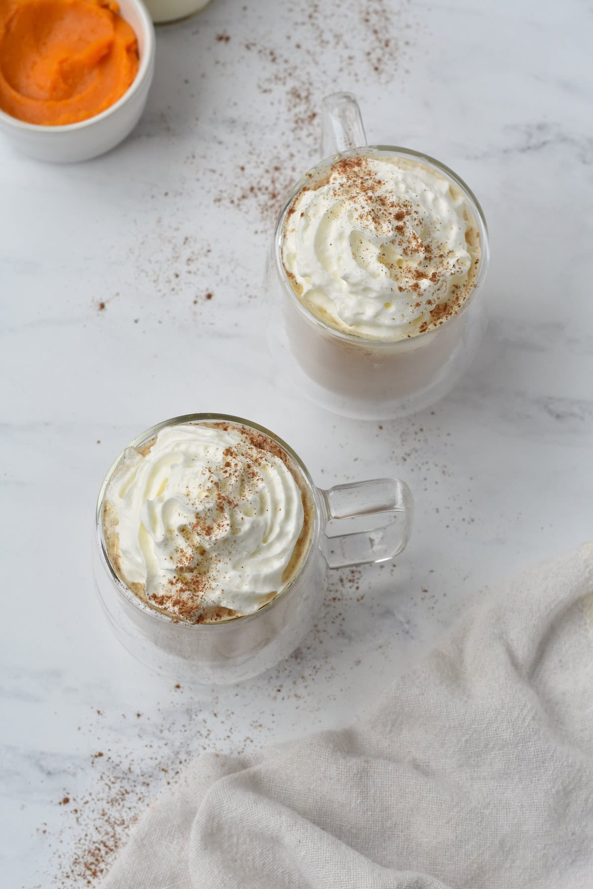 Two pumpkin spice lattes shot from above with whipped cream on top.