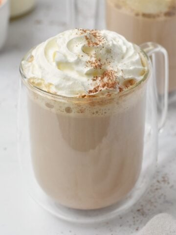 Pumpkin spice latte in glass cup with whipped cream on top.