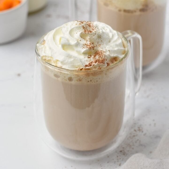 Pumpkin spice latte in glass cup with whipped cream on top.